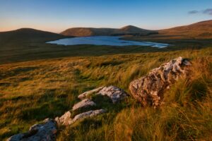 Breathtaking view of Northern Ireland's landscape with lake, hills, and grassland at sunset.